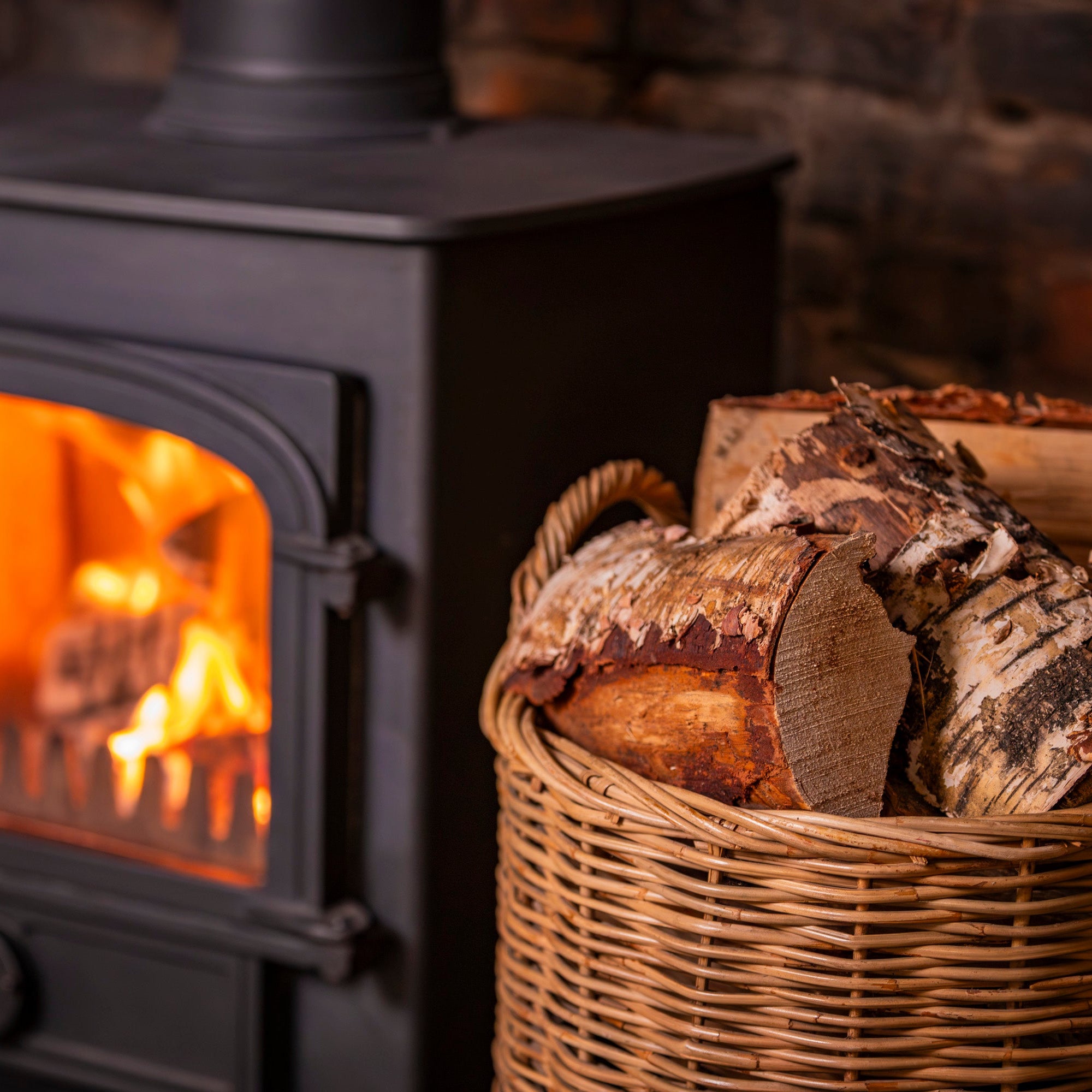 Wood-burning stove with glowing fire and a basket of sevenoaks firewood logs.