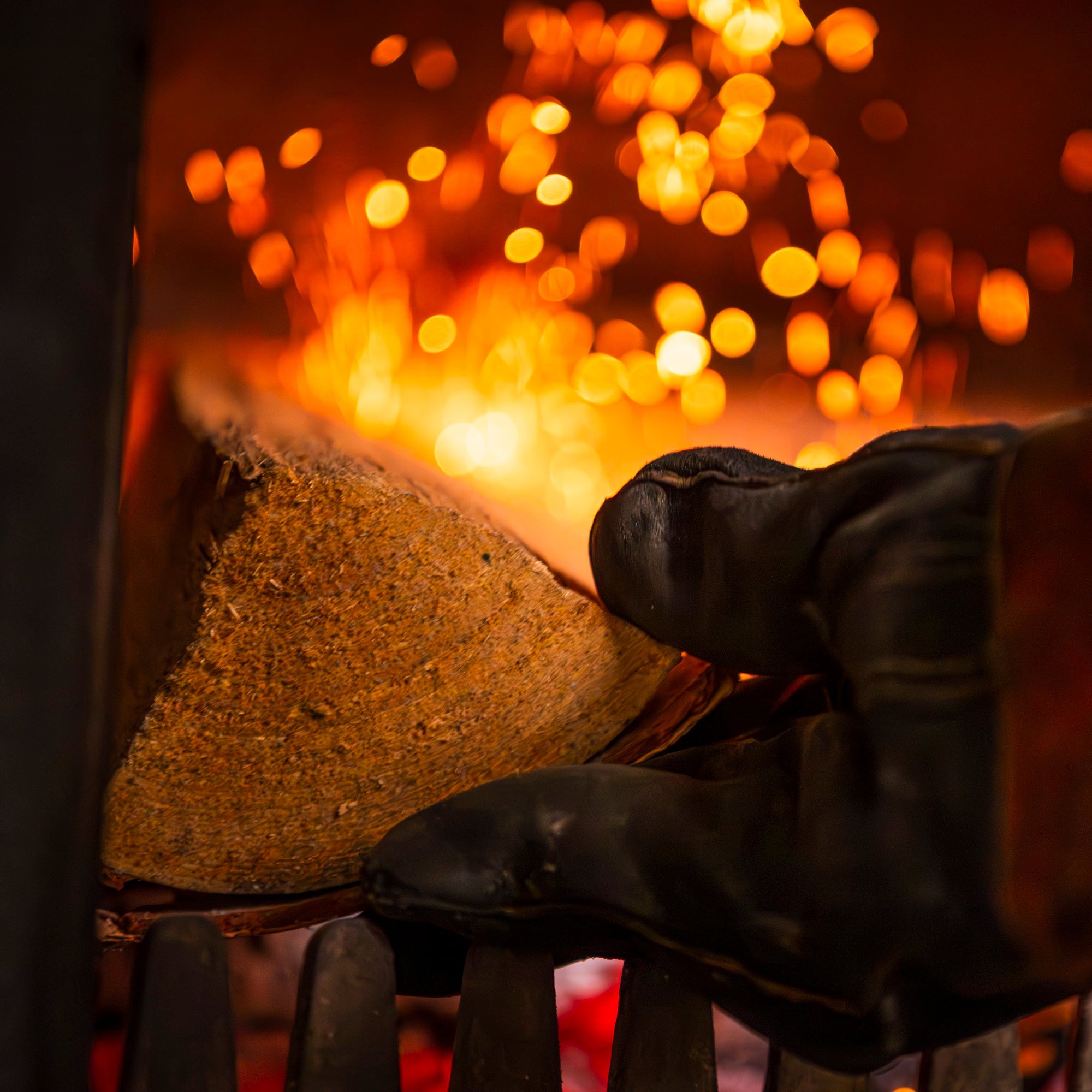 Black glove holding a piece of wood in front of a fire