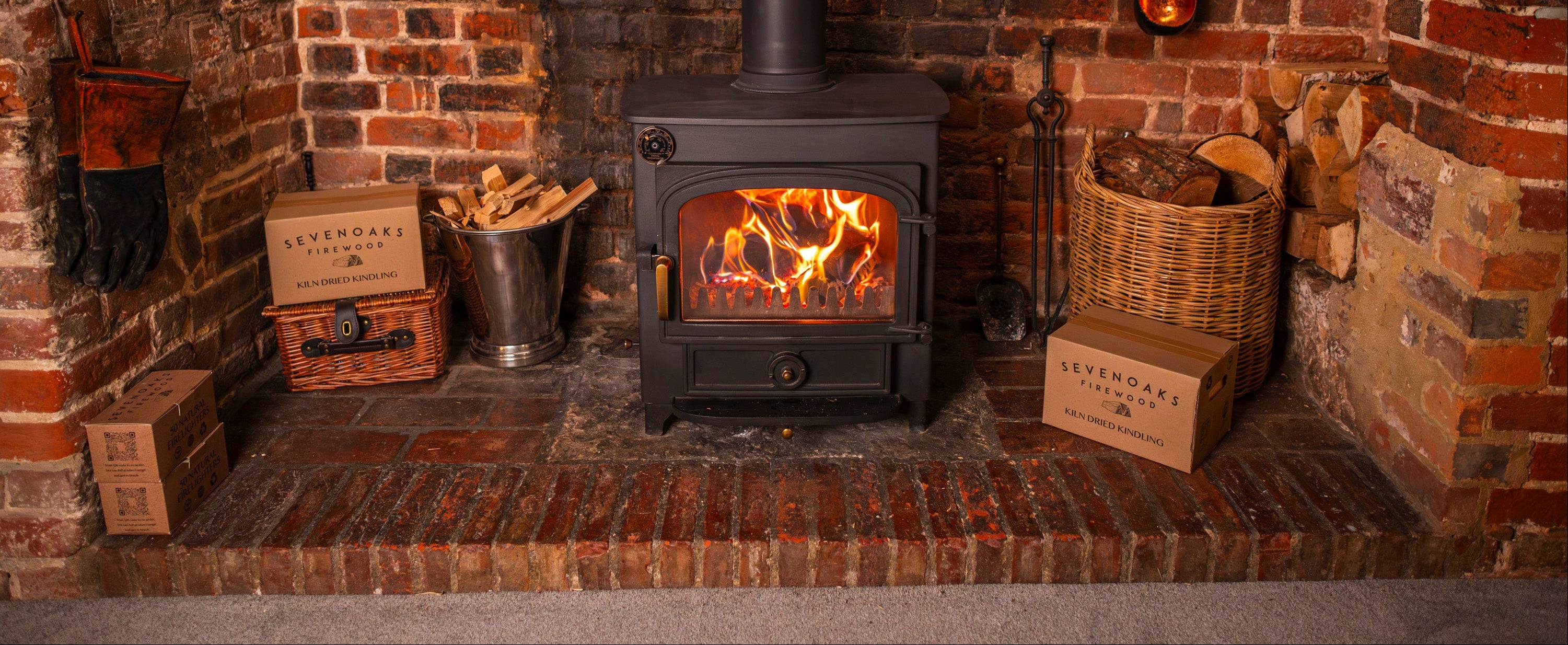 Sevenoaks Firewood brick fireplace with a lit stove and various rustic items around it.